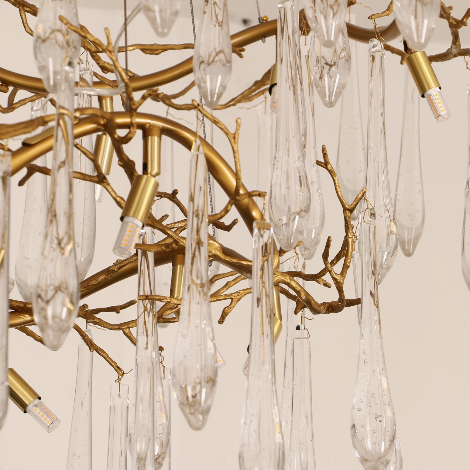 Side angled close-up of brass waterfall chandelier showing mounted LED bulb, polished gold branch texture, and hanging teardrop crystal pendants