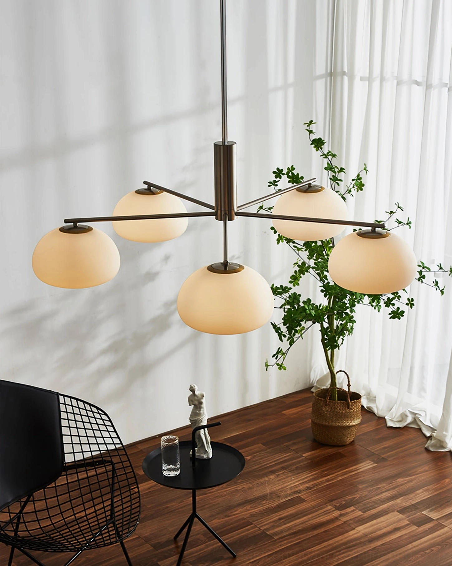 Six-arm sputnik Briette chandelier with brass frame and warm opal glass shades in bright space with wooden floor and potted plant