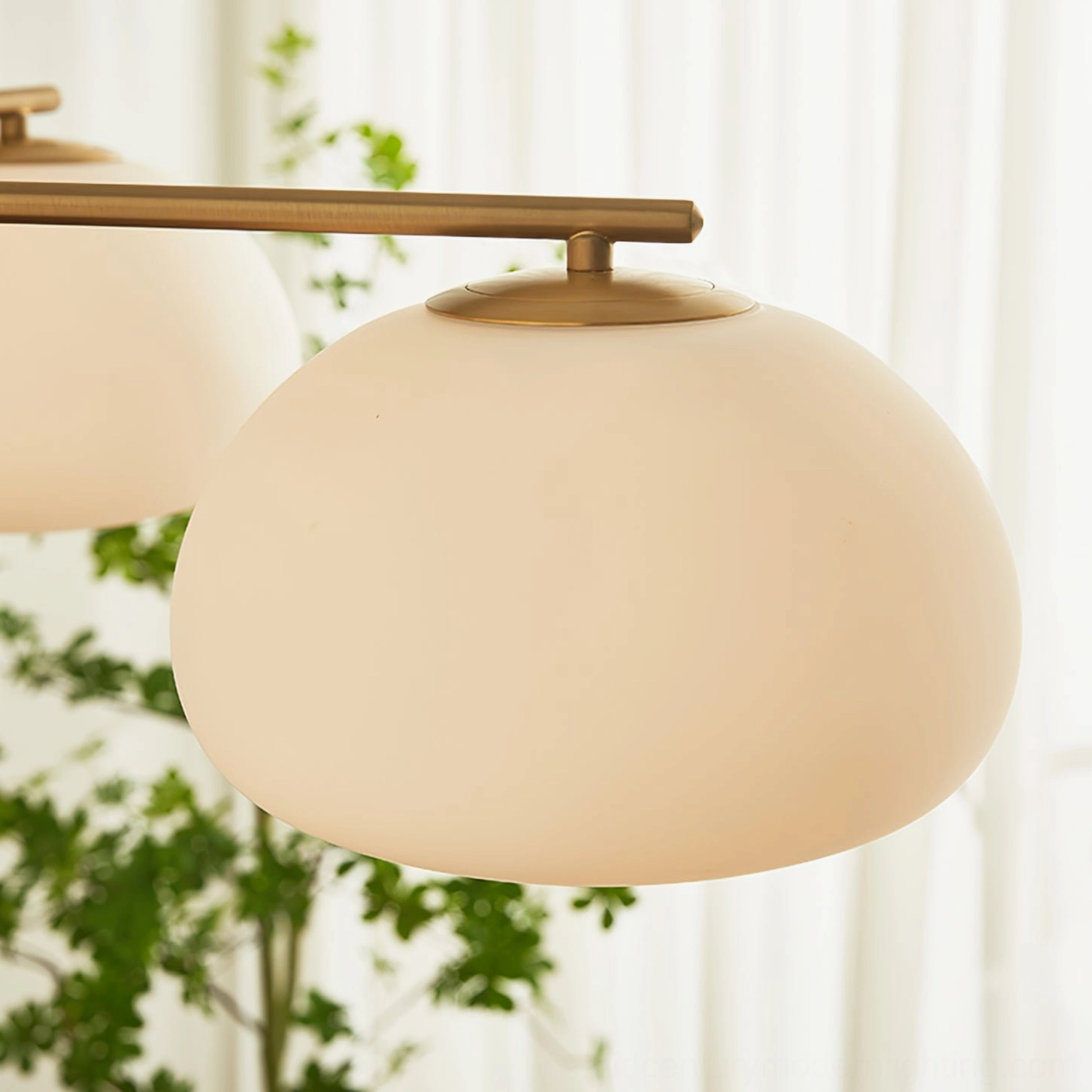 Close-up detail of Briette chandelier frosted glass shade with warm minimalist home decor, sheer curtains and greenery background