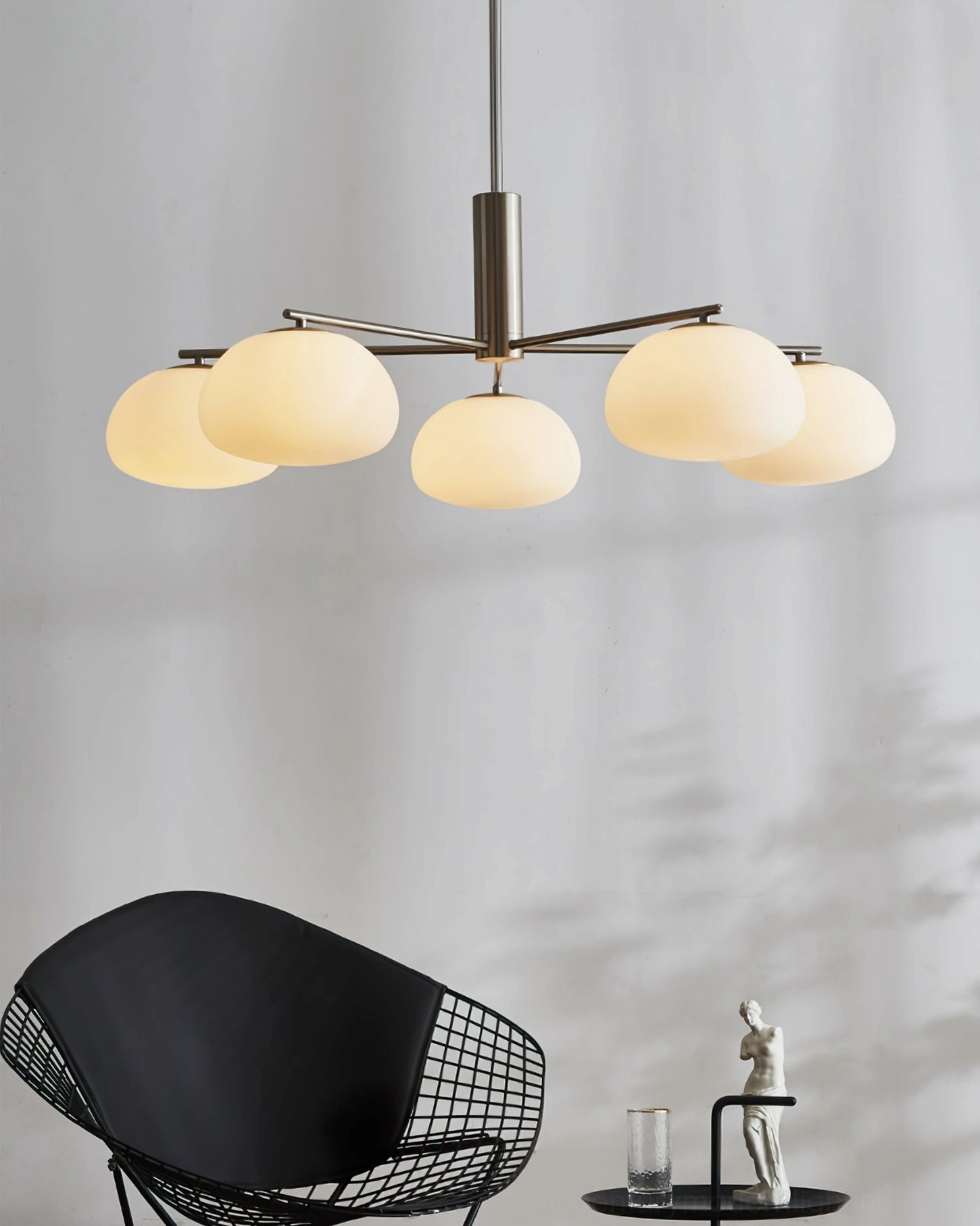 Brass sputnik chandelier Briette hanging in minimalist Nordic studio with warm glowing opal glass shades and accent chair