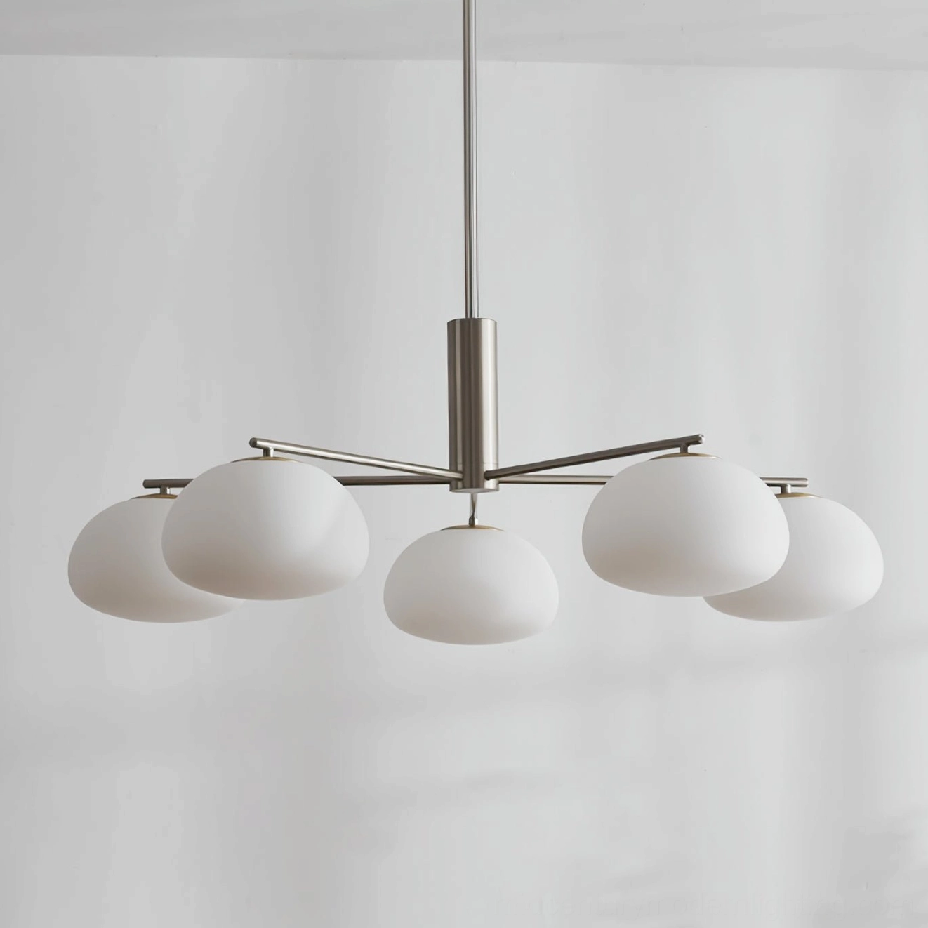 Silver sputnik chandelier Briette with matte finish and frosted white glass globes hanging against sheer curtain background