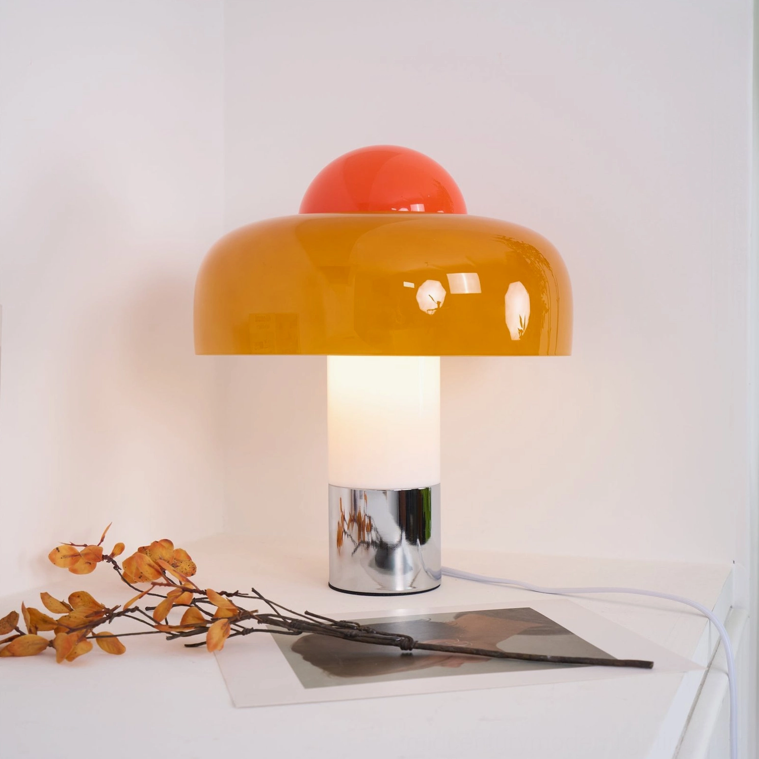 Brumbry table lamp on white tabletop with dried twigs and photo print, showcasing chrome base and power cord