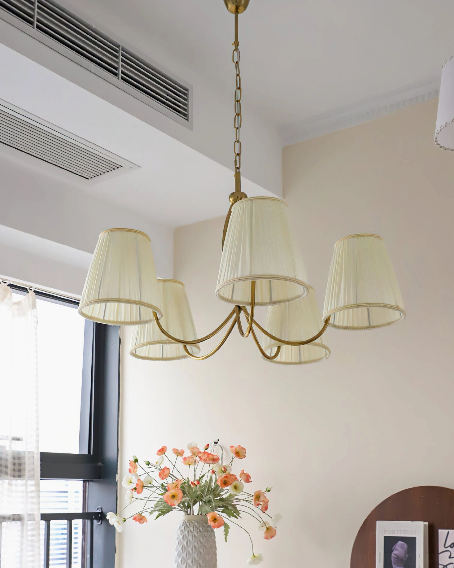 Unlit Calistoga brass chandelier in room with large windows and orange floral centerpiece below
