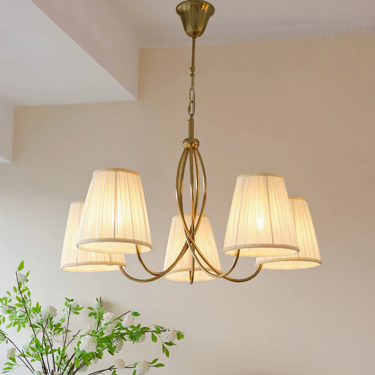 Calistoga brass chandelier illuminated in warm light, low-angle shot showing curved frame and soft glow on cream wall