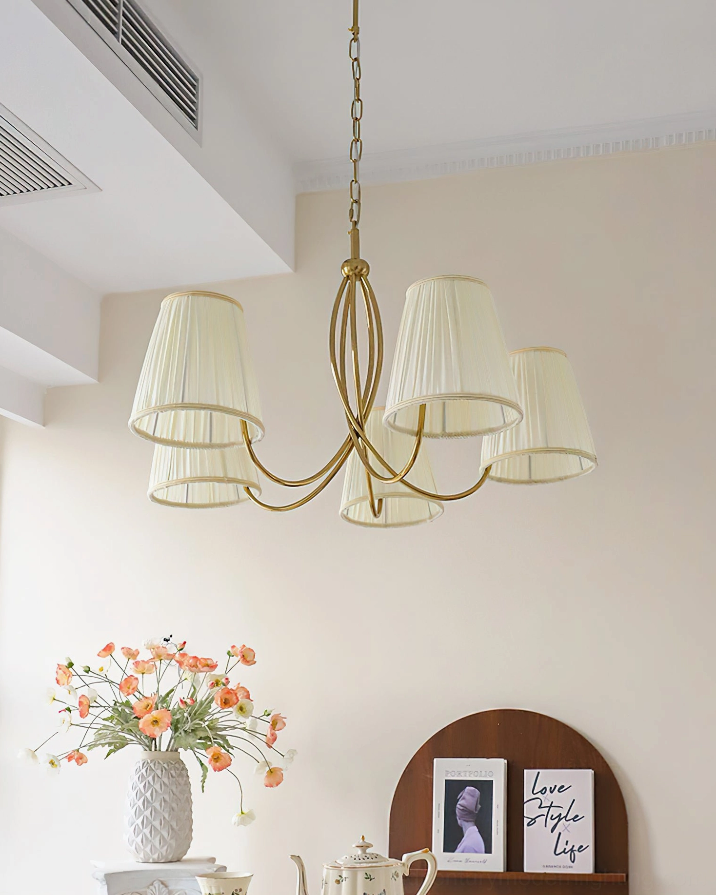 Calistoga 5-light chandelier with brass frame and layered pleated fabric shades, side three-quarter view with orange flowers