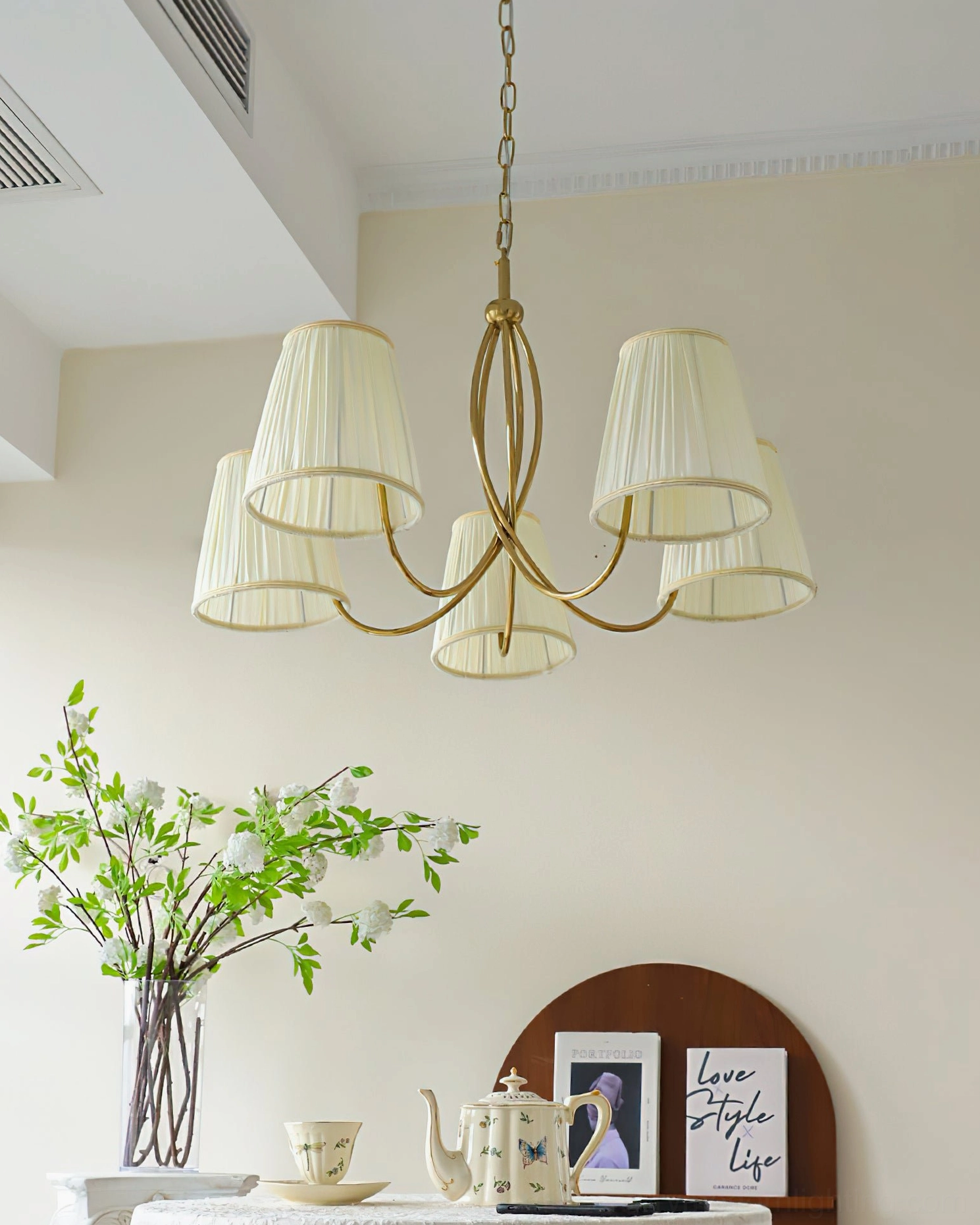 Unlit Calistoga 5-light chandelier with pleated off-white shades, three-quarter front view in minimalist interior