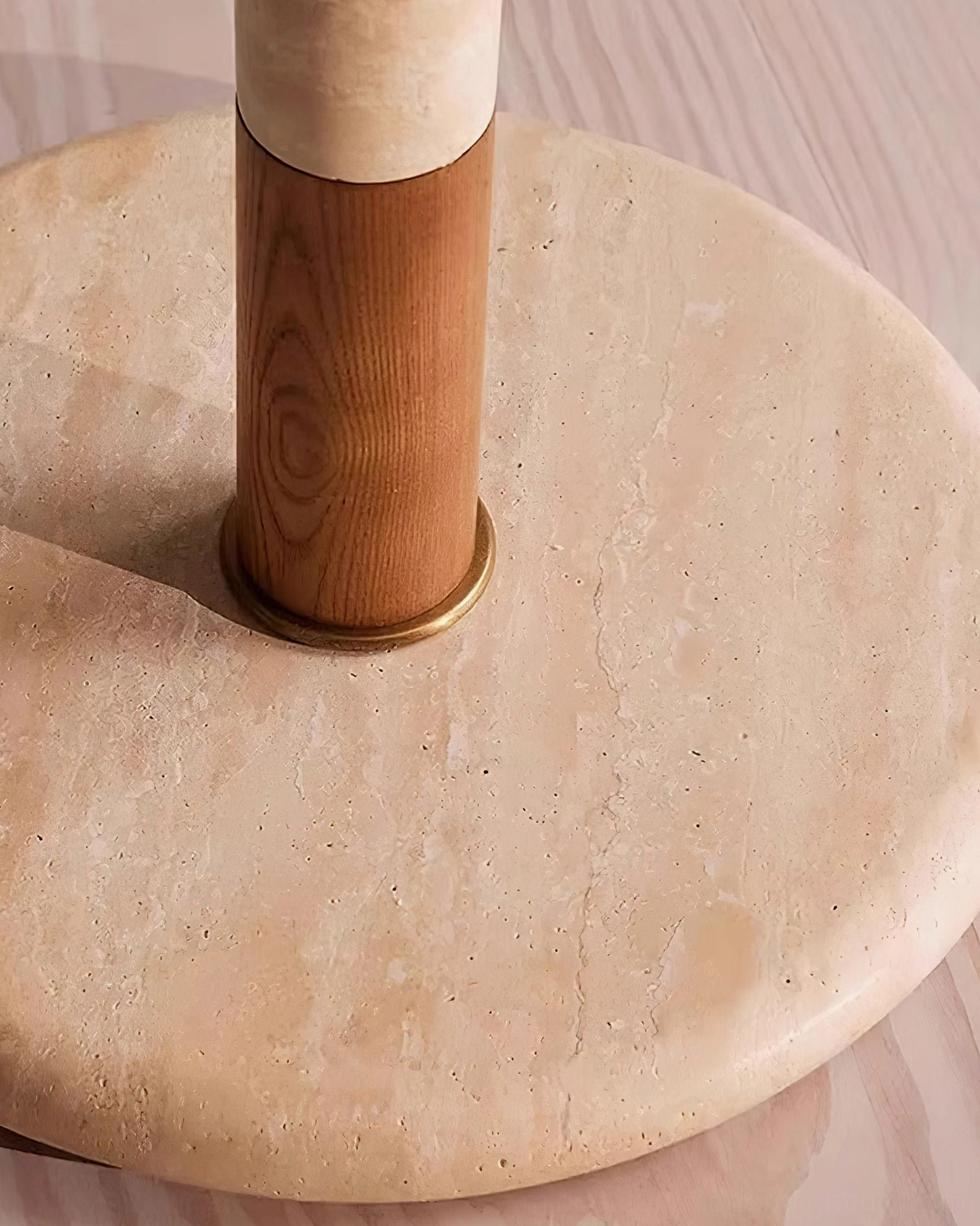 Overhead close-up of Calypso floor lamp travertine marble round base with brass accent ring on light wood floor