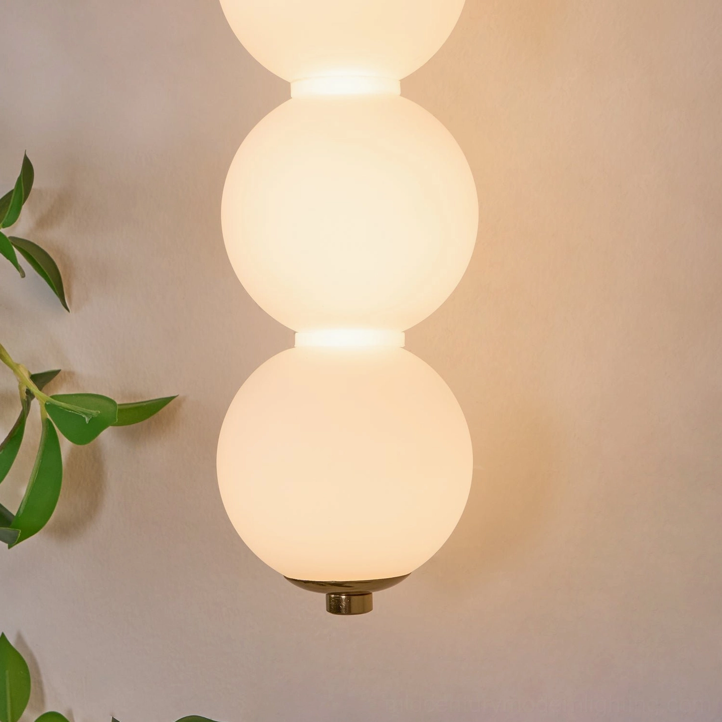 Close-up of illuminated Candied Haws sconce frosted glass globes with warm light and brass accents