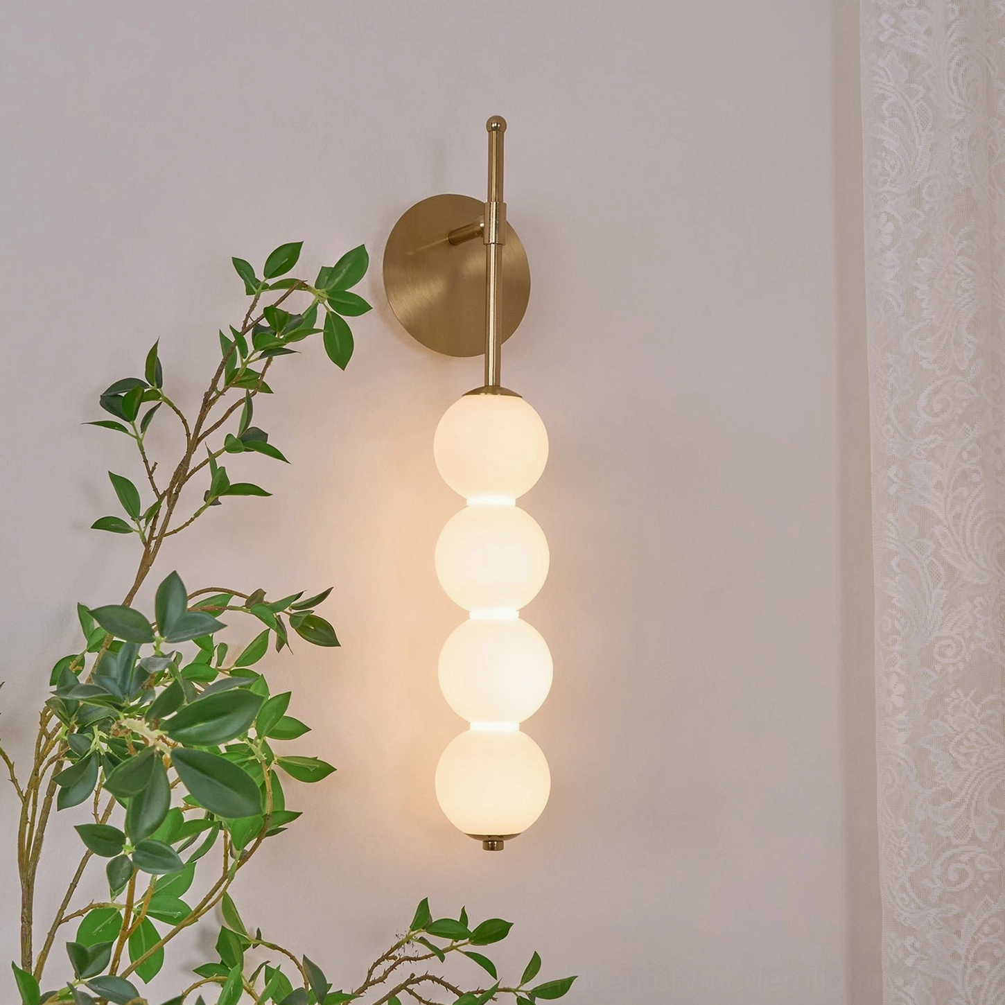 Lit Candied Haws four-globe wall light casting warm glow with brass hardware against green foliage backdrop
