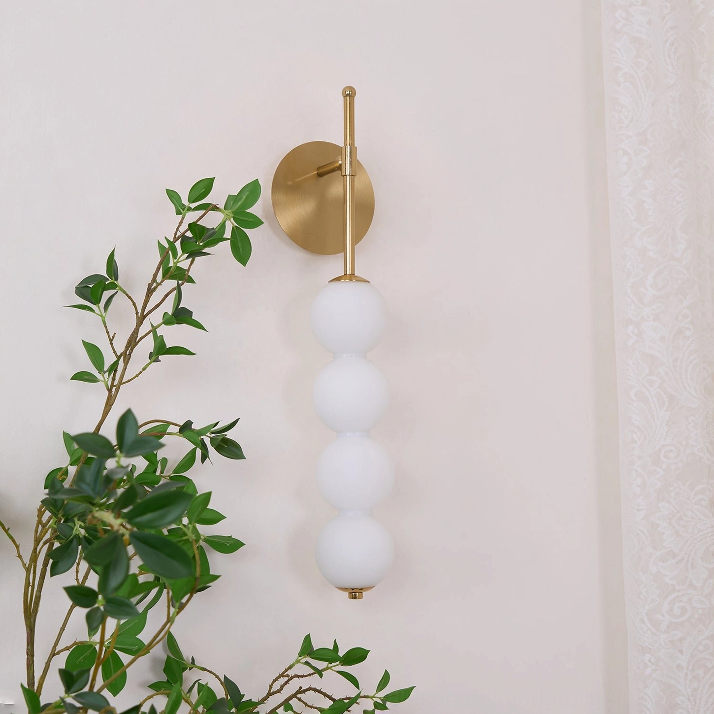 Unlit Candied Haws wall sconce mounted on green foliage wall, side view showing brass hardware and frosted glass spheres