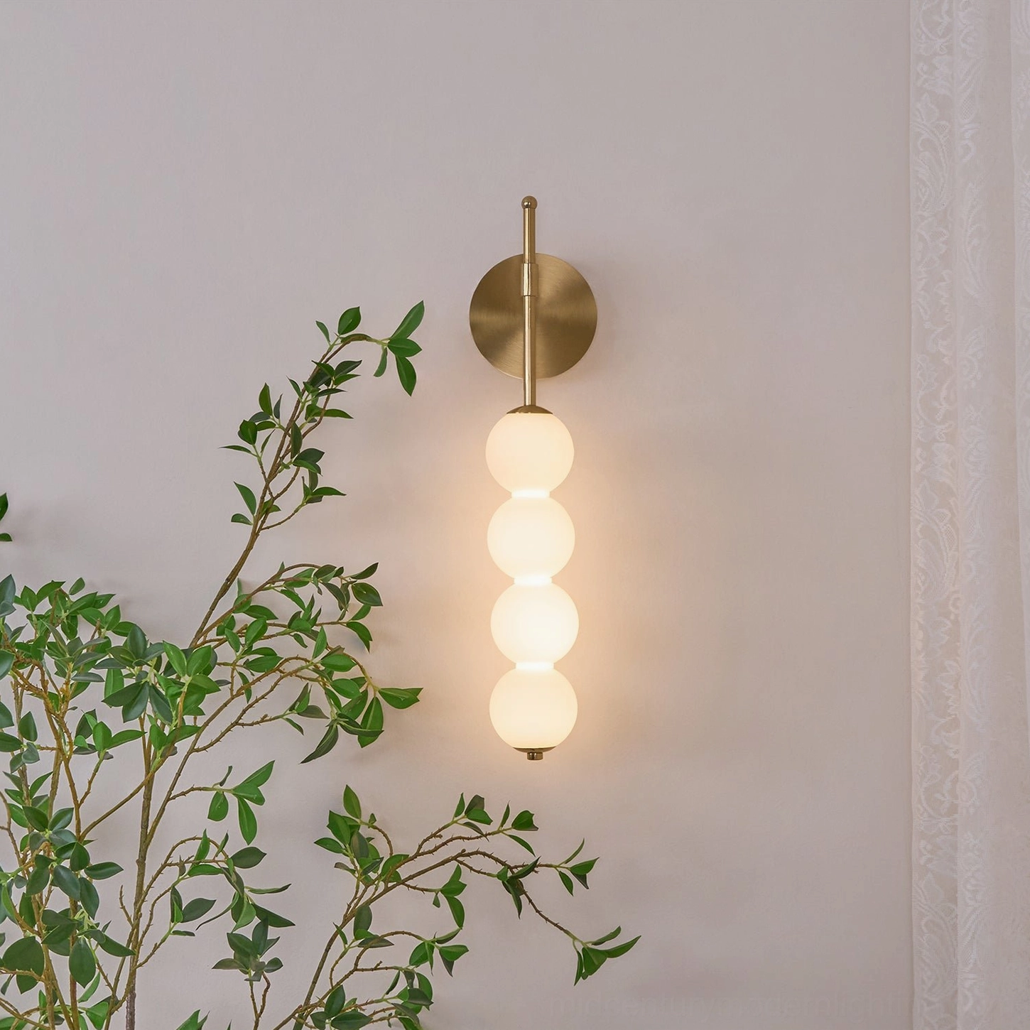 Candied Haws four-globe wall lamp illuminated with soft warm light, brass base mounted on indoor wall