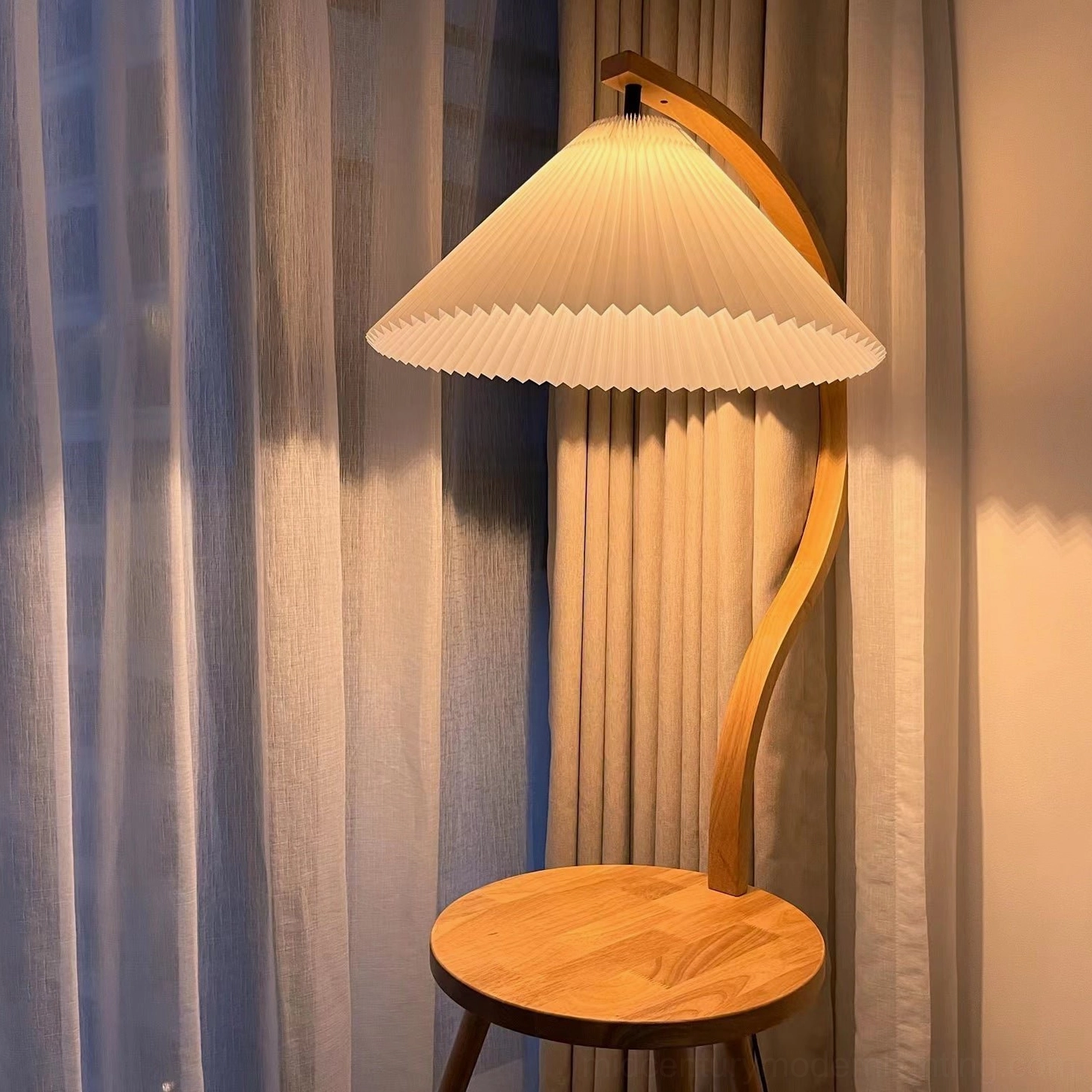 Caprani floor lamp with wooden side table creating warm ambient lighting in living room at night with curtain backdrop