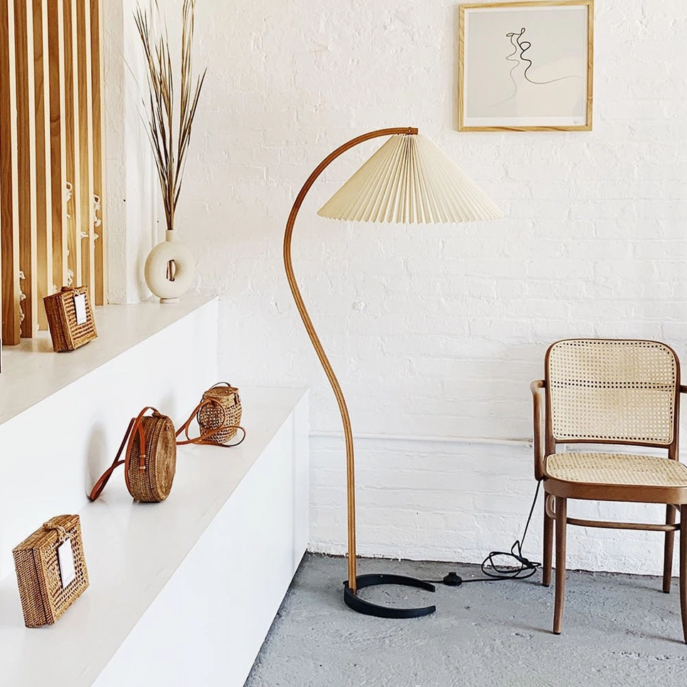 Caprani floor lamp eye-level view in minimalist entryway with rattan dining chair and decorative shelf