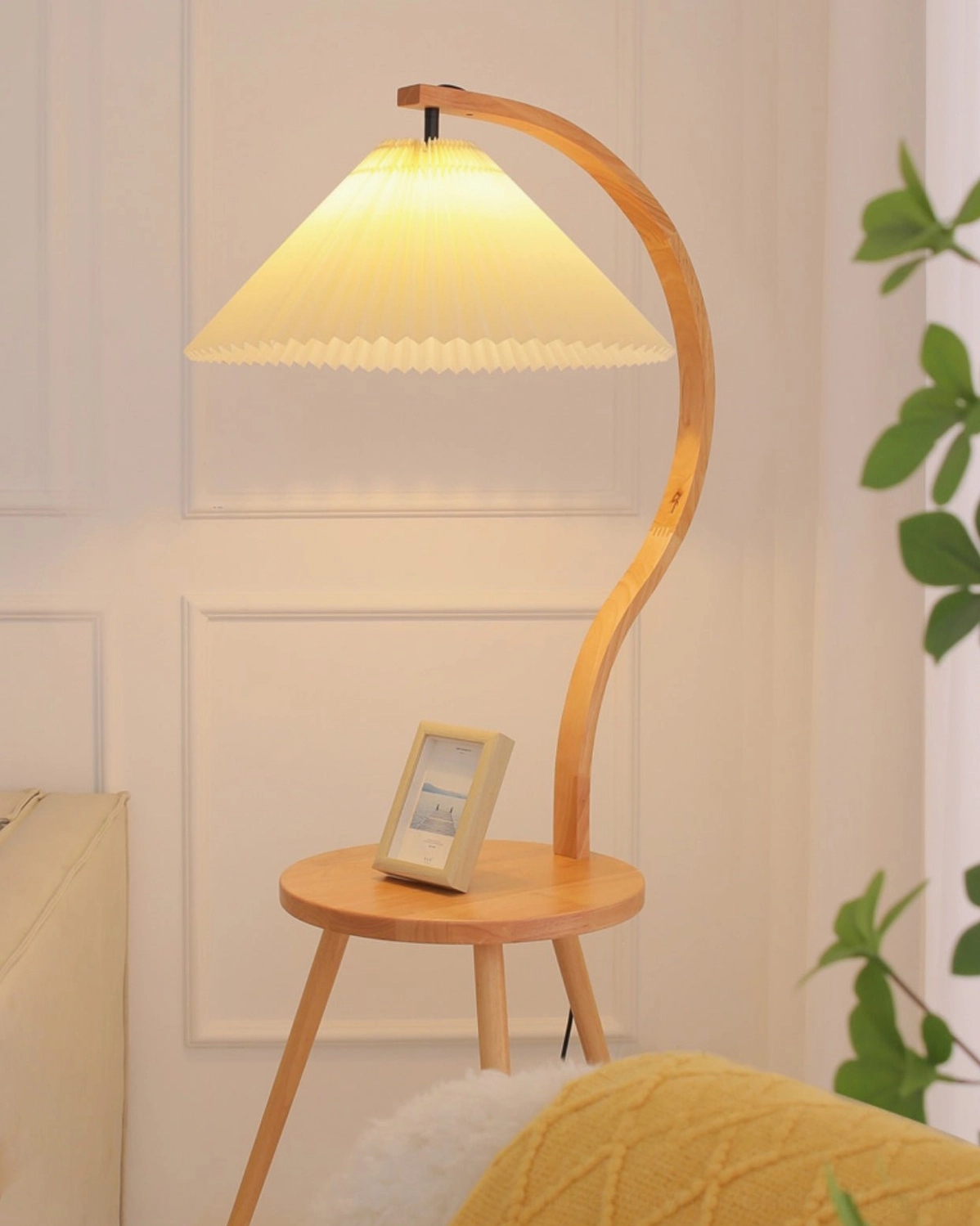 Standing Caprani floor lamp with illuminated pleated shade in living room corner with small photo frame decor