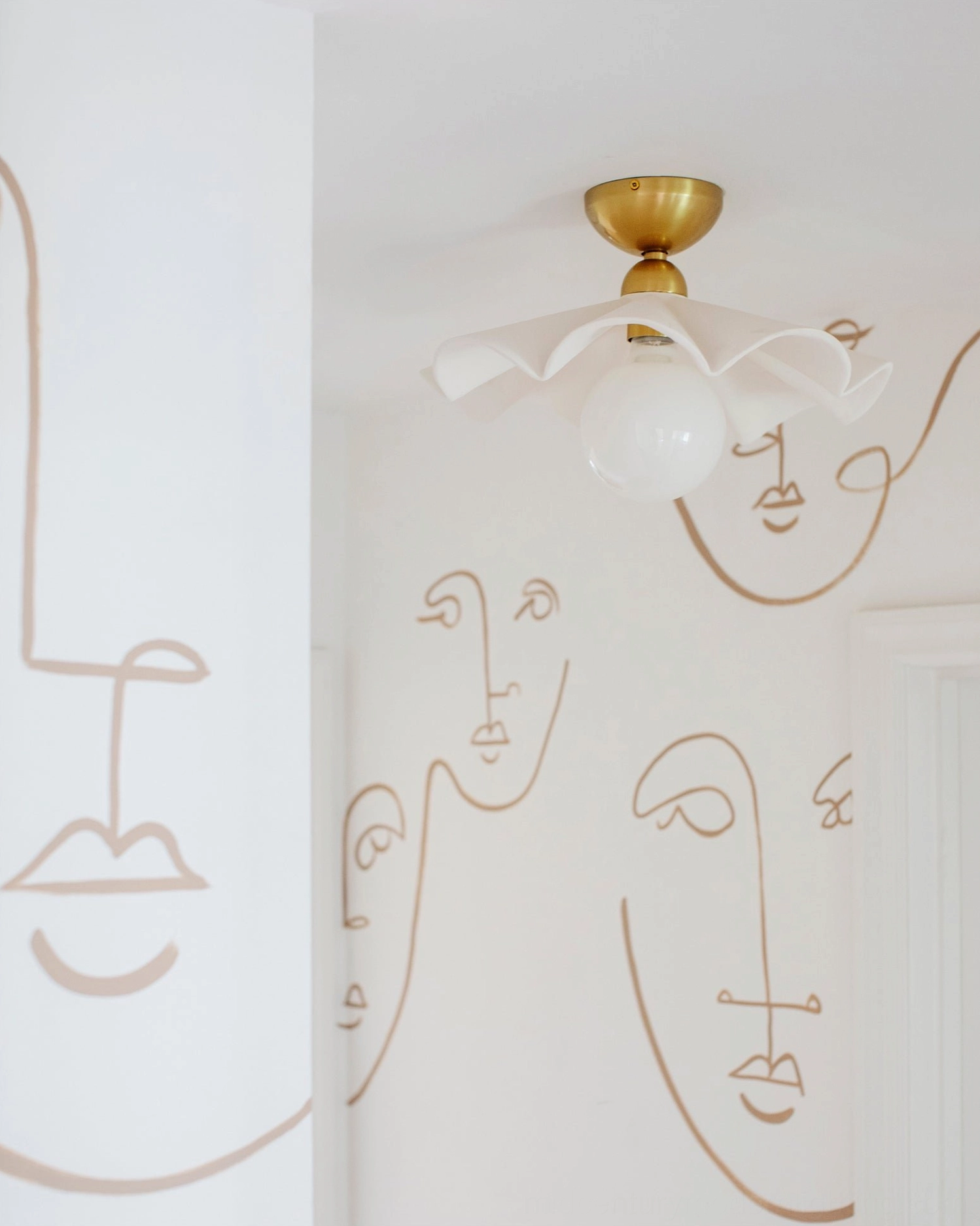 Close-up side view of Capri flush mount ceiling lamp with minimalist face line art wallpaper accent wall detail