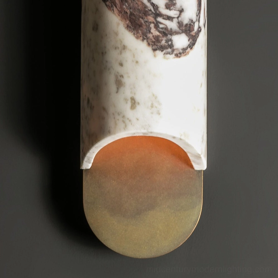 Close-up detail of capsule wall lamp showing marble veining texture, warm amber LED glow, and brushed brass trim
