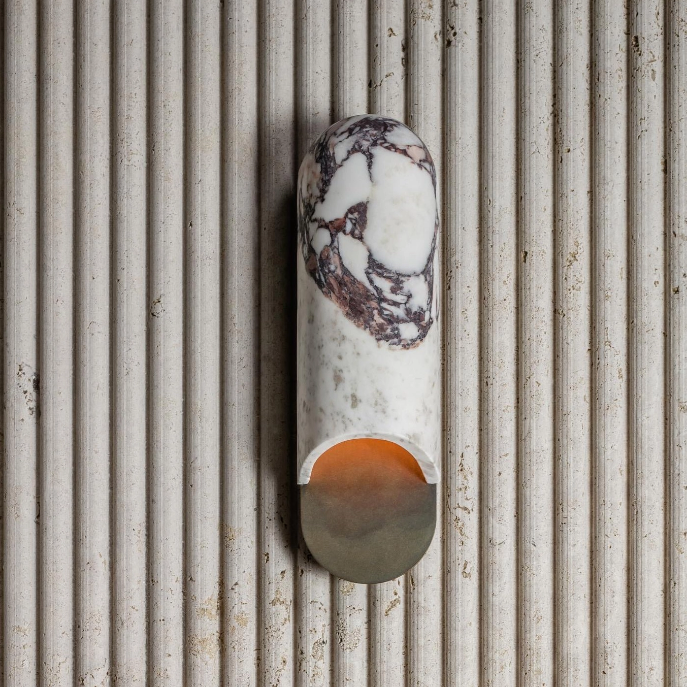 Overhead view of beige travertine capsule wall lamp mounted on fluted accent wall with ambient warm light