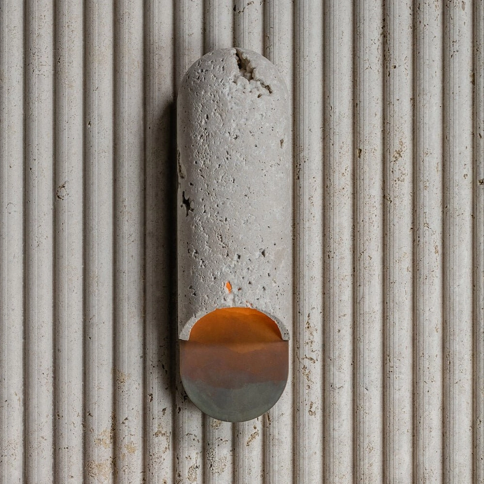 Top-down detail of porous travertine capsule wall lamp showing texture and subtle warm ambient light