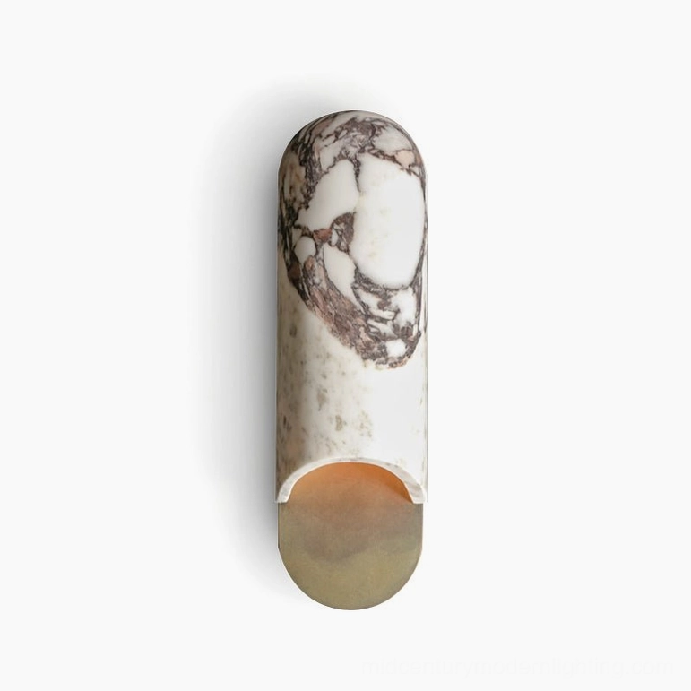 Front view of white marble capsule wall lamp with metallic brass base and warm glowing LED on studio white backdrop