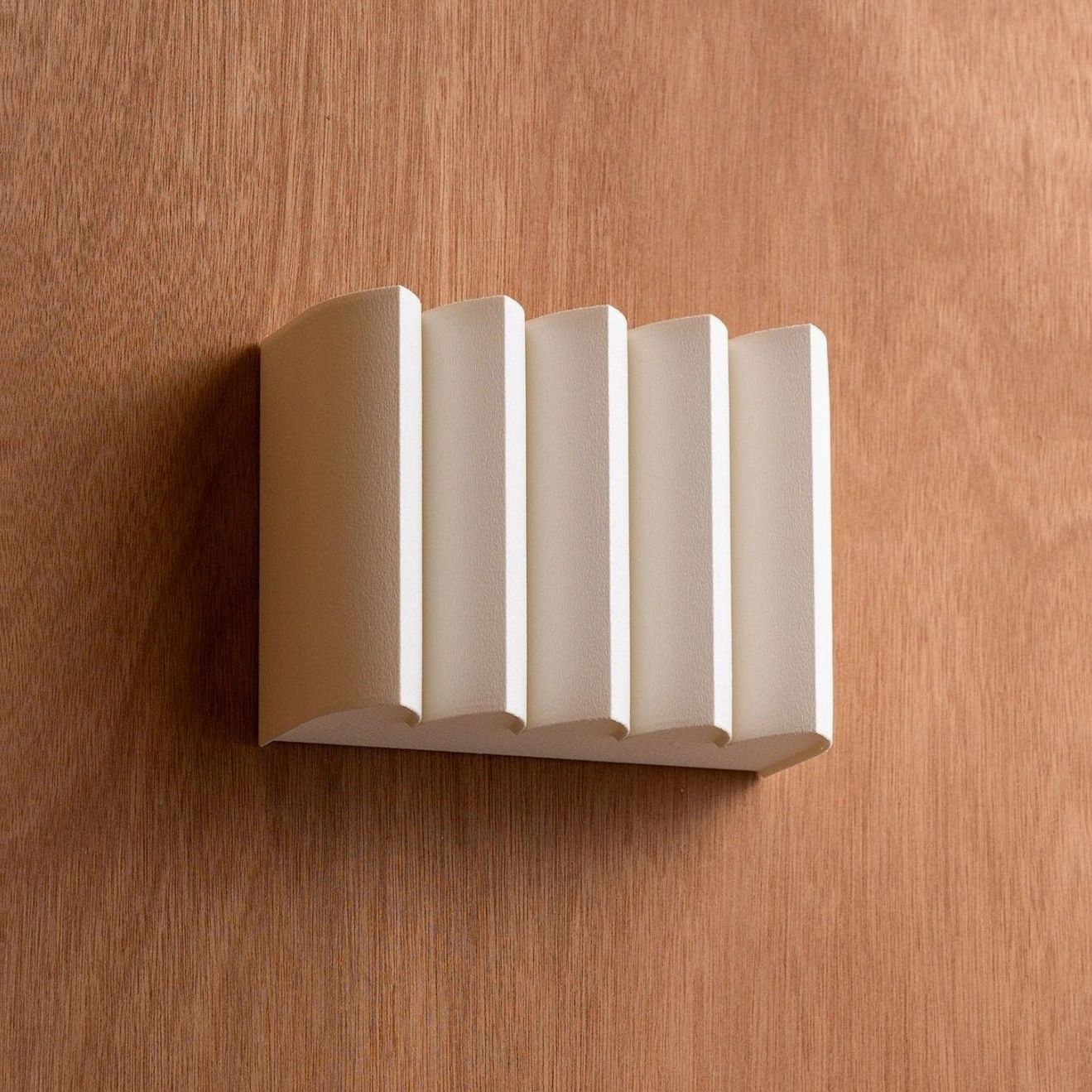 Matte white ribbed wall sconce with stepped rectangular shape on medium brown wood wall