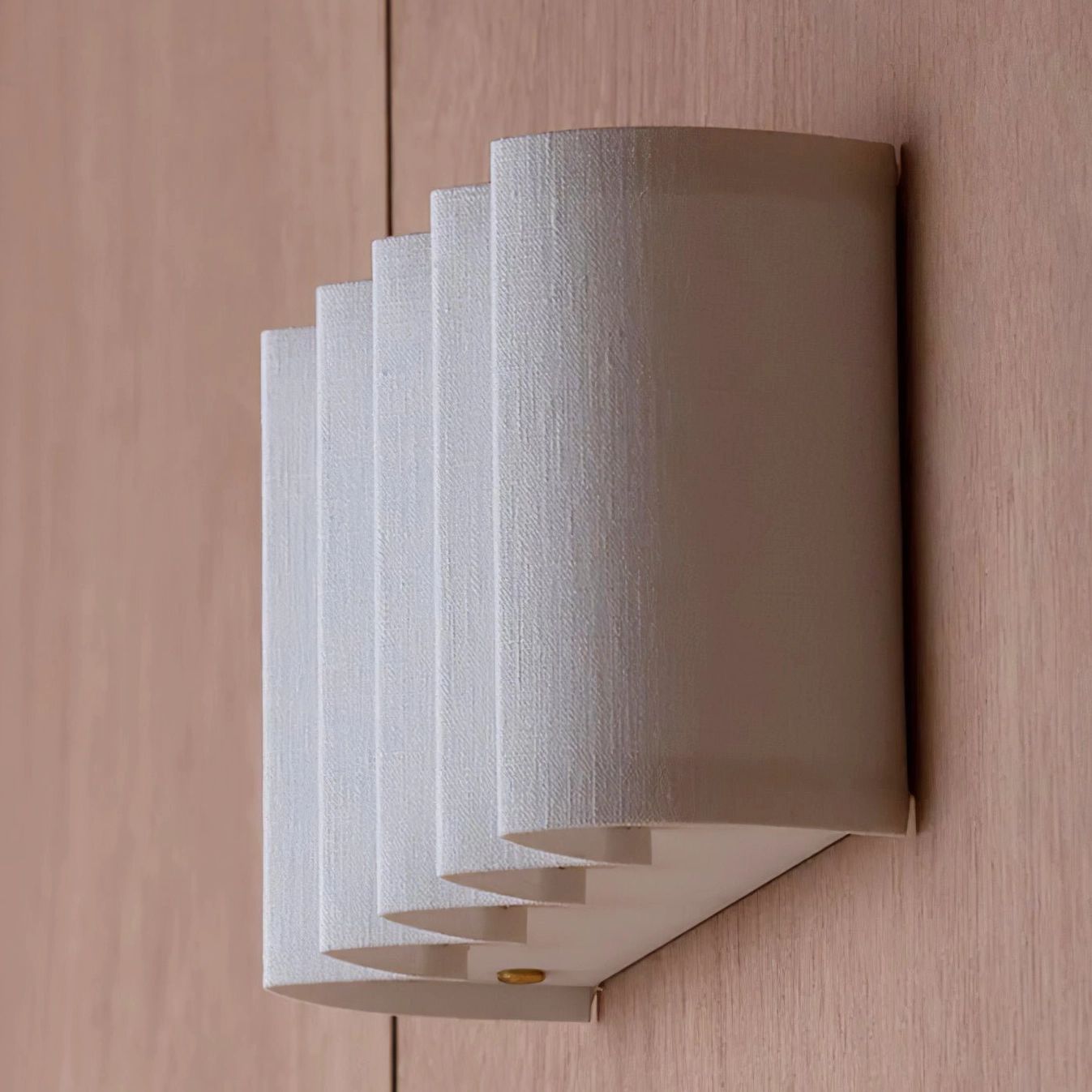 Large ribbed fabric wall lamp with angled side-front view on warm light wood wall