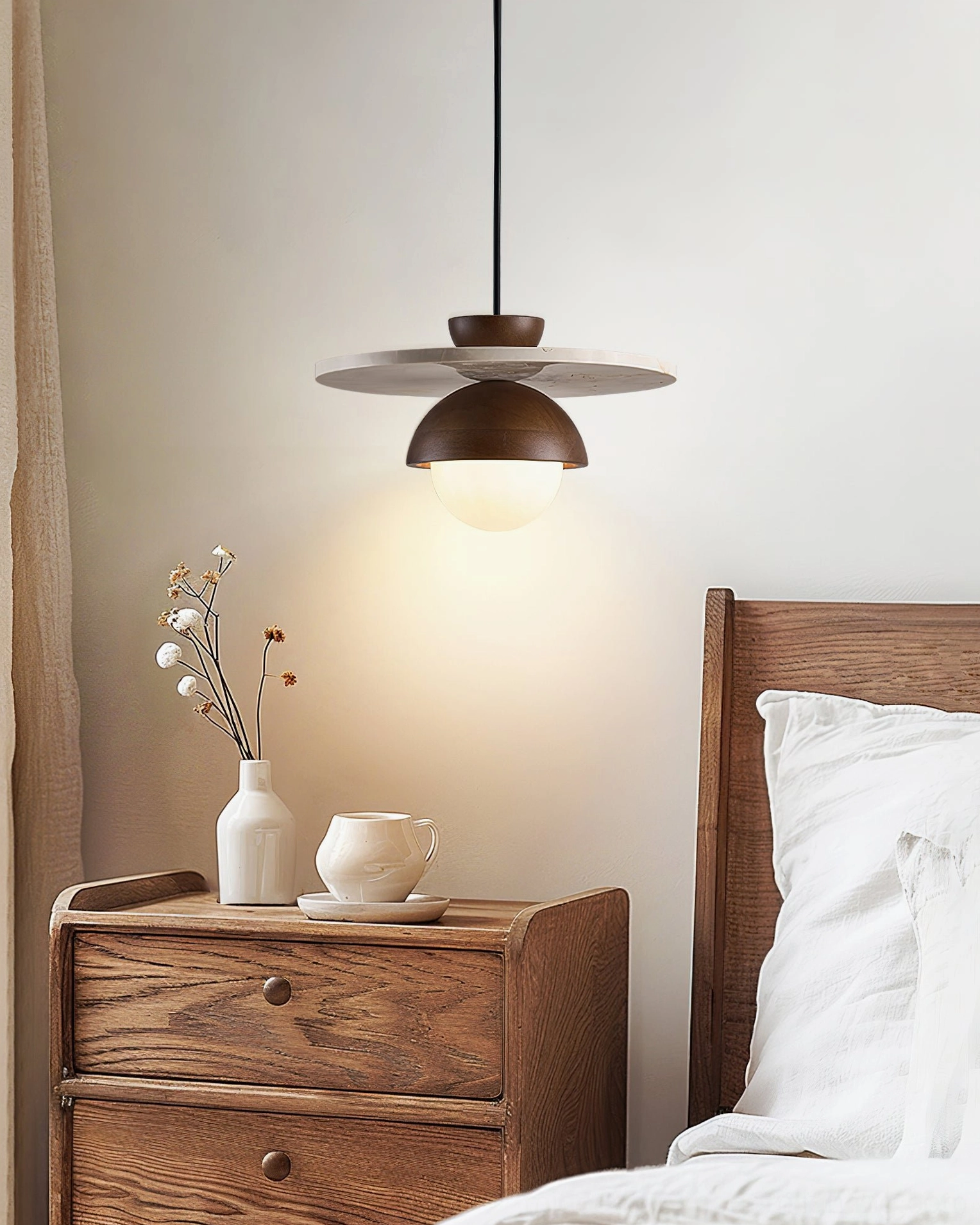 Cassini pendant lamp installed above wooden nightstand in warm bedroom with soft ambient lighting