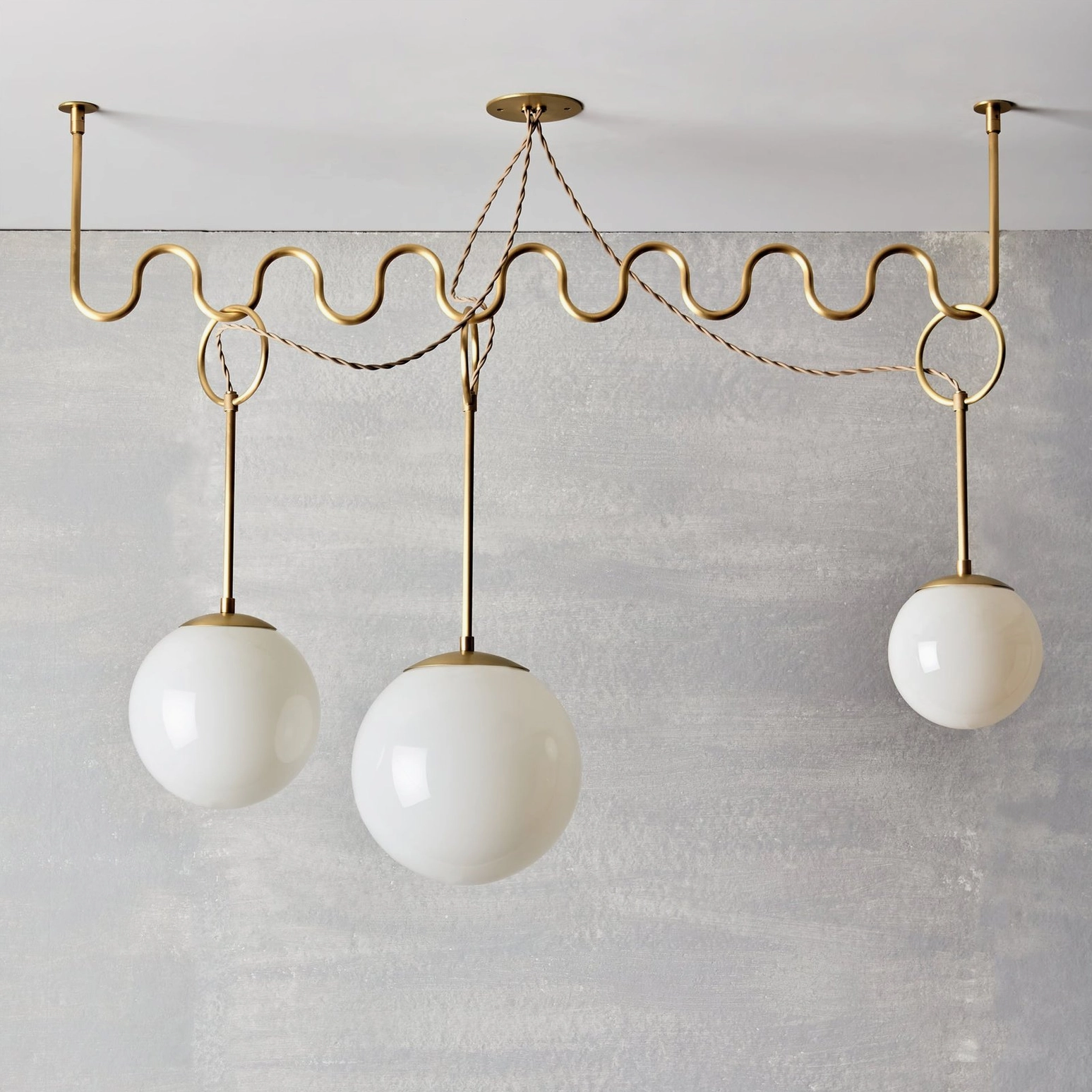 Full view of Cecil wavy brass chandelier illuminated, showing warm ambient glow and sculptural design