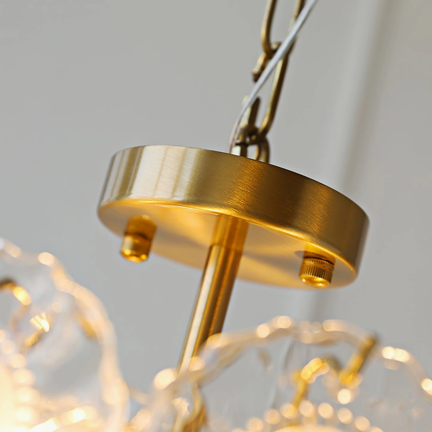 Close-up detail of brass ceiling lamp suspension hardware showing polished metal chain and mounting