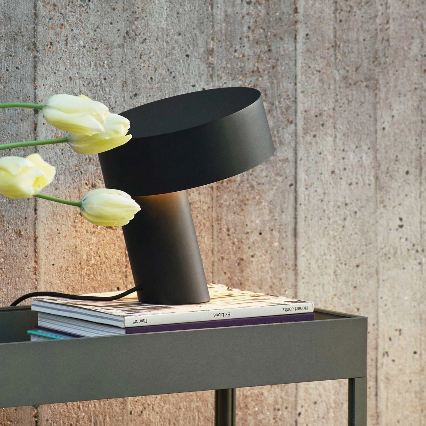 Matte black Celia angular lamp on industrial console table with books and yellow tulips, modern styling