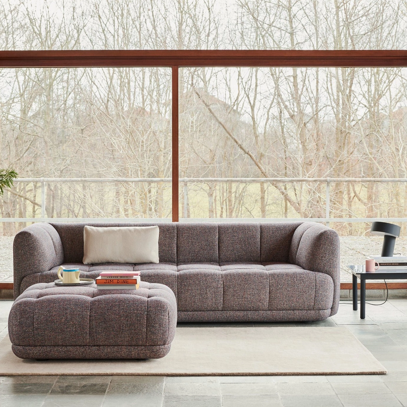 White Celia angular table lamp in bright modern living room with floor-to-ceiling windows and gray tufted sofa