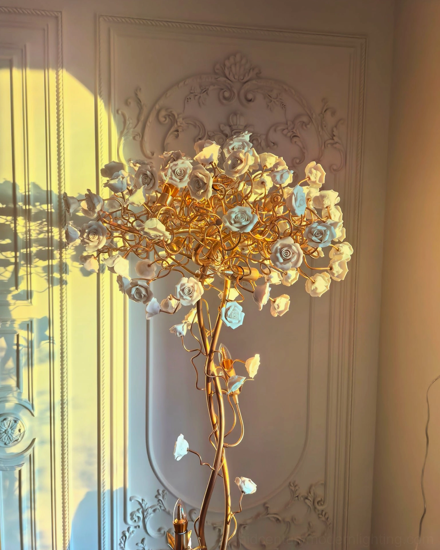Side close-up of ceramic flower lamp with blue-tinted ceramic flower accents casting floral shadow on carved European wall