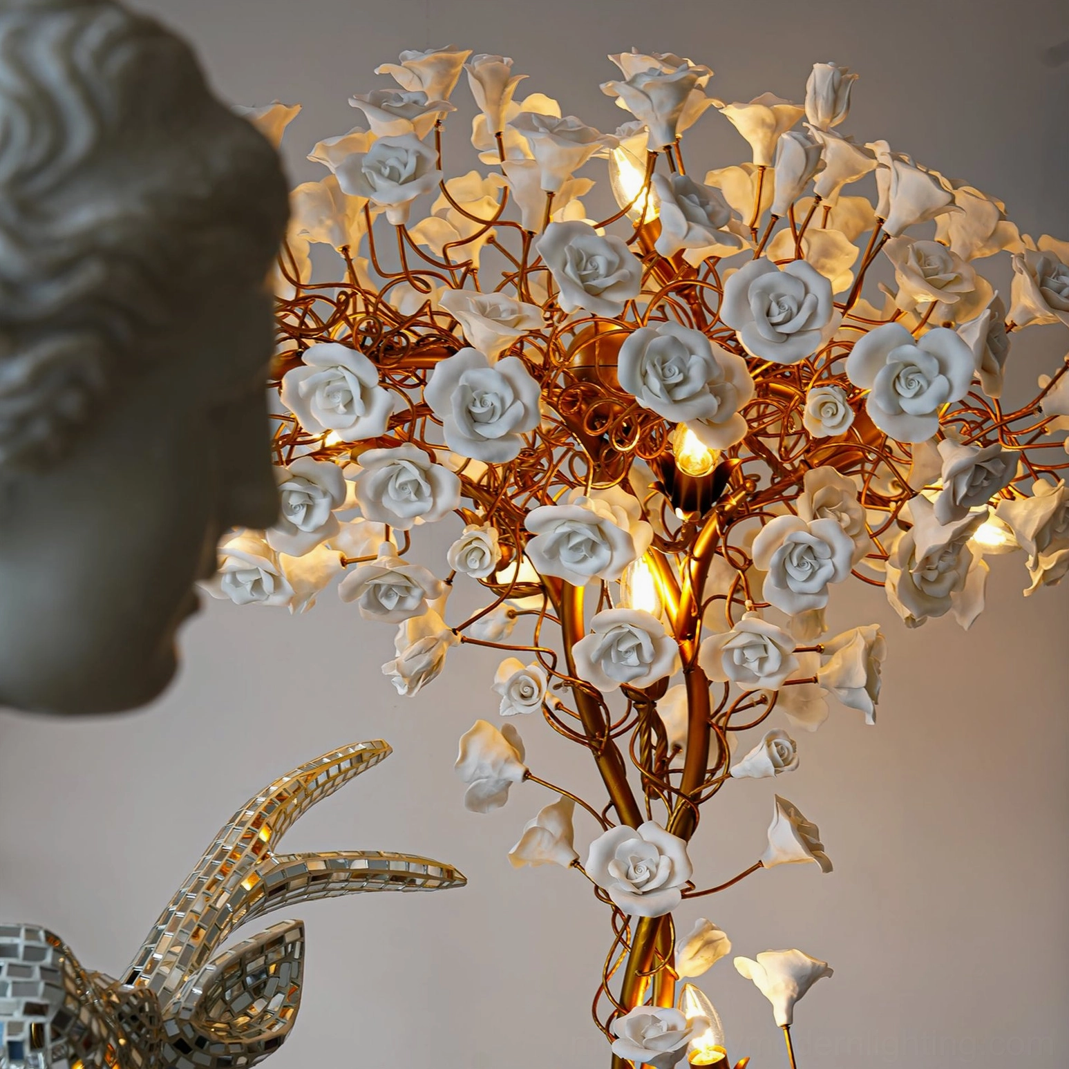 Close-up detail of ceramic flower lamp head showing gold metal branches and white ceramic roses with warm glowing lights