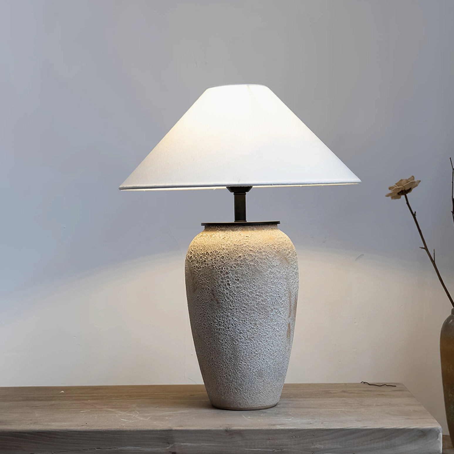 Ceramic table lamp with minimalist styling and single dried flower stem on neutral background