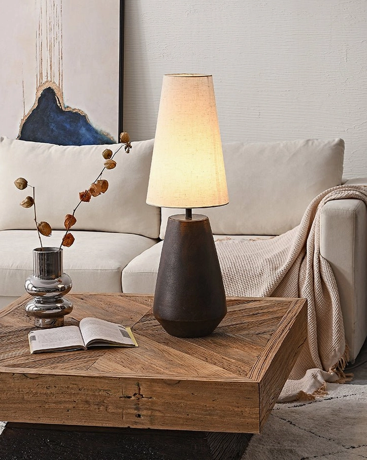 Handcrafted ceramic table lamp beside sofa with dried floral decor and wooden coffee table, showcasing rustic contemporary home interior