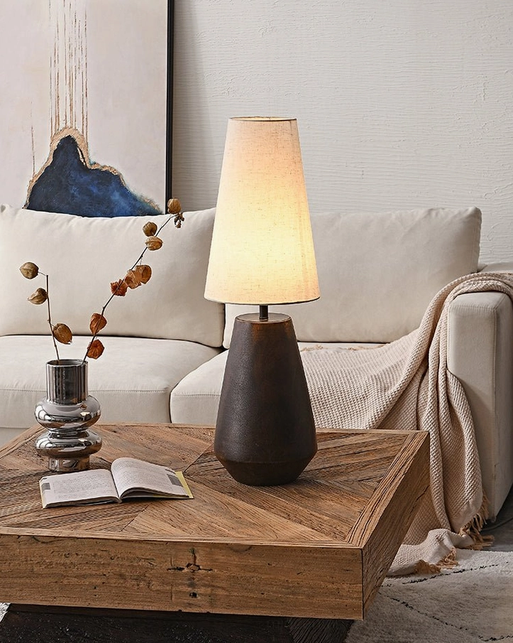 Ceramic tapered table lamp illuminating cozy living room space with open book on coffee table, creating warm ambient lighting