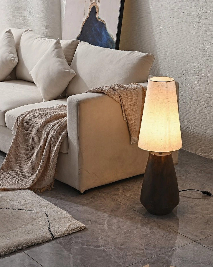 Tapered ceramic table lamp positioned beside sofa on modern marble floor, demonstrating neutral contemporary home decor styling