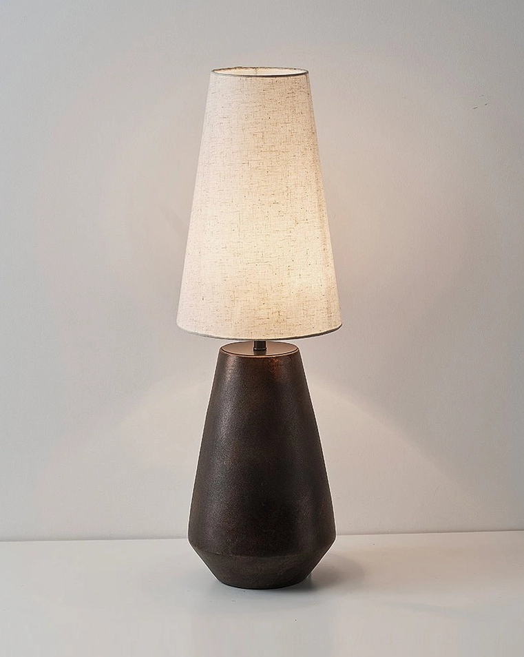 Ceramic tapered table lamp with warm glowing fabric shade, studio front view on white background, highlighting design form and light diffusion