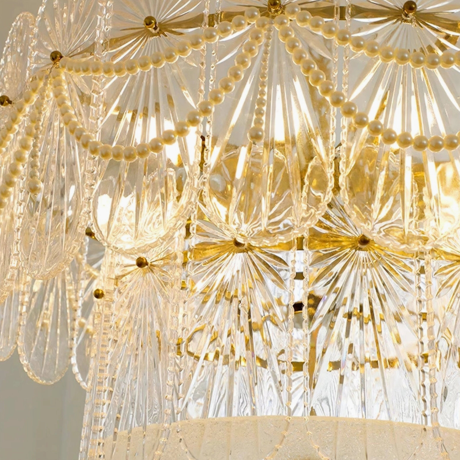 Close-up detail of Art Deco glass chandelier showing gold floral accents, pearl beads, and internal LED bulbs