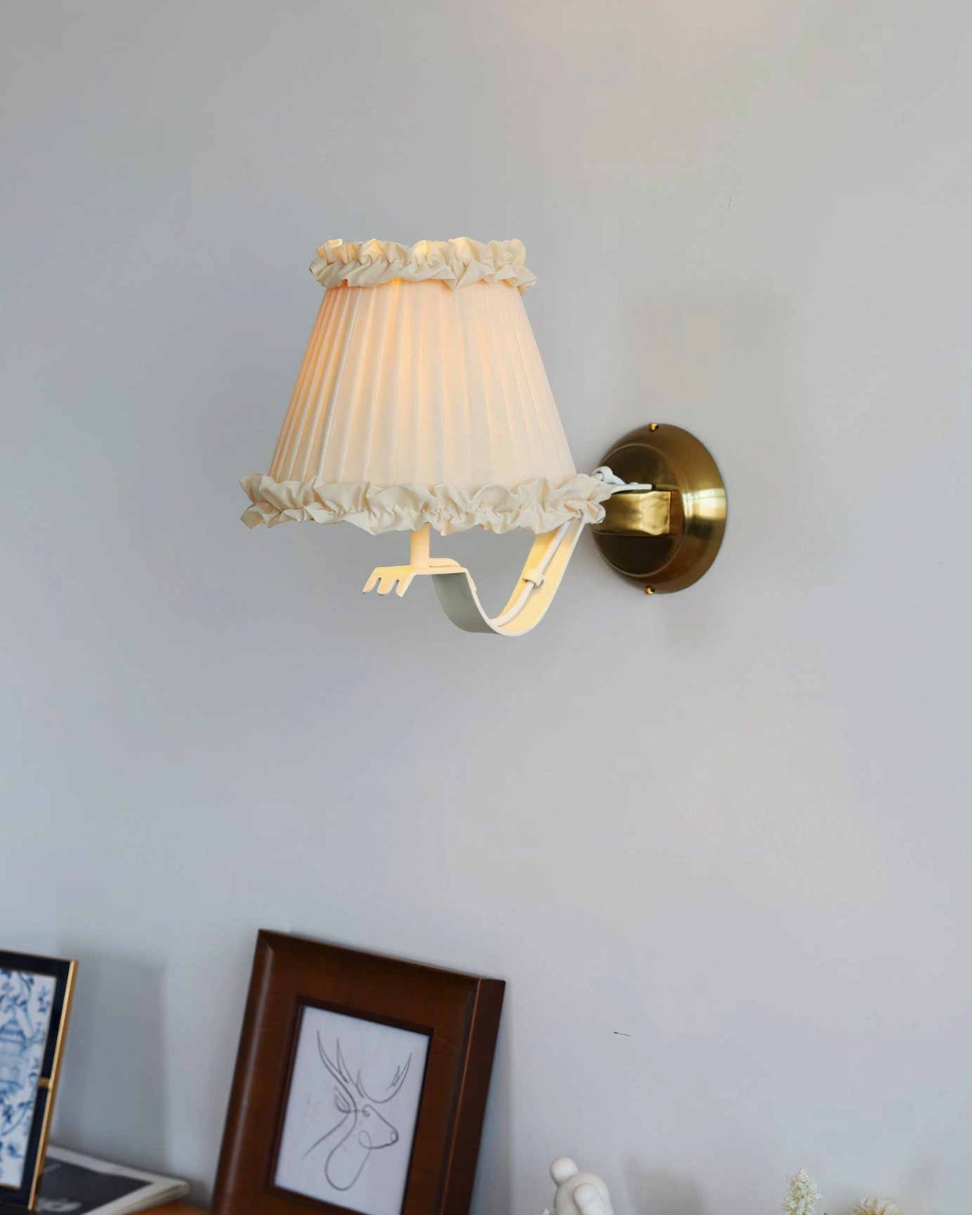 Chantal wall sconce with cream pleated shade and brass hardware on light gray wall with artwork