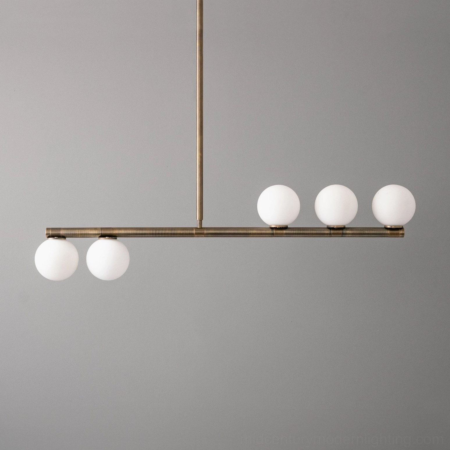 Mid-century modern linear pendant chandelier featuring five matte white glass spheres suspended on bronze metal rod, frontal view