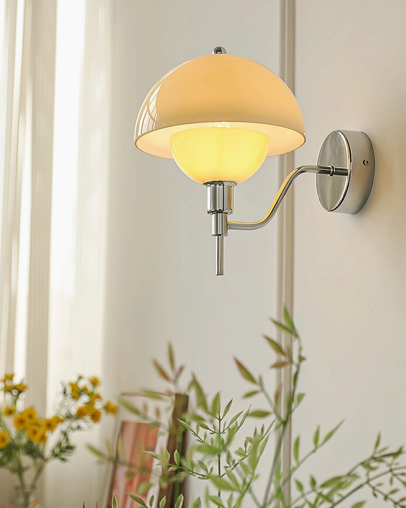 Warm-lit chrome orb wall lamp with amber glass shade in home setting surrounded by green plants and modern decor