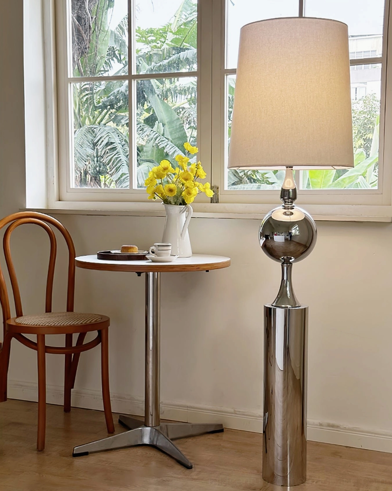 Chrome floor lamp in dining nook beside wooden table and bentwood chair with yellow floral arrangement - mid-century setting