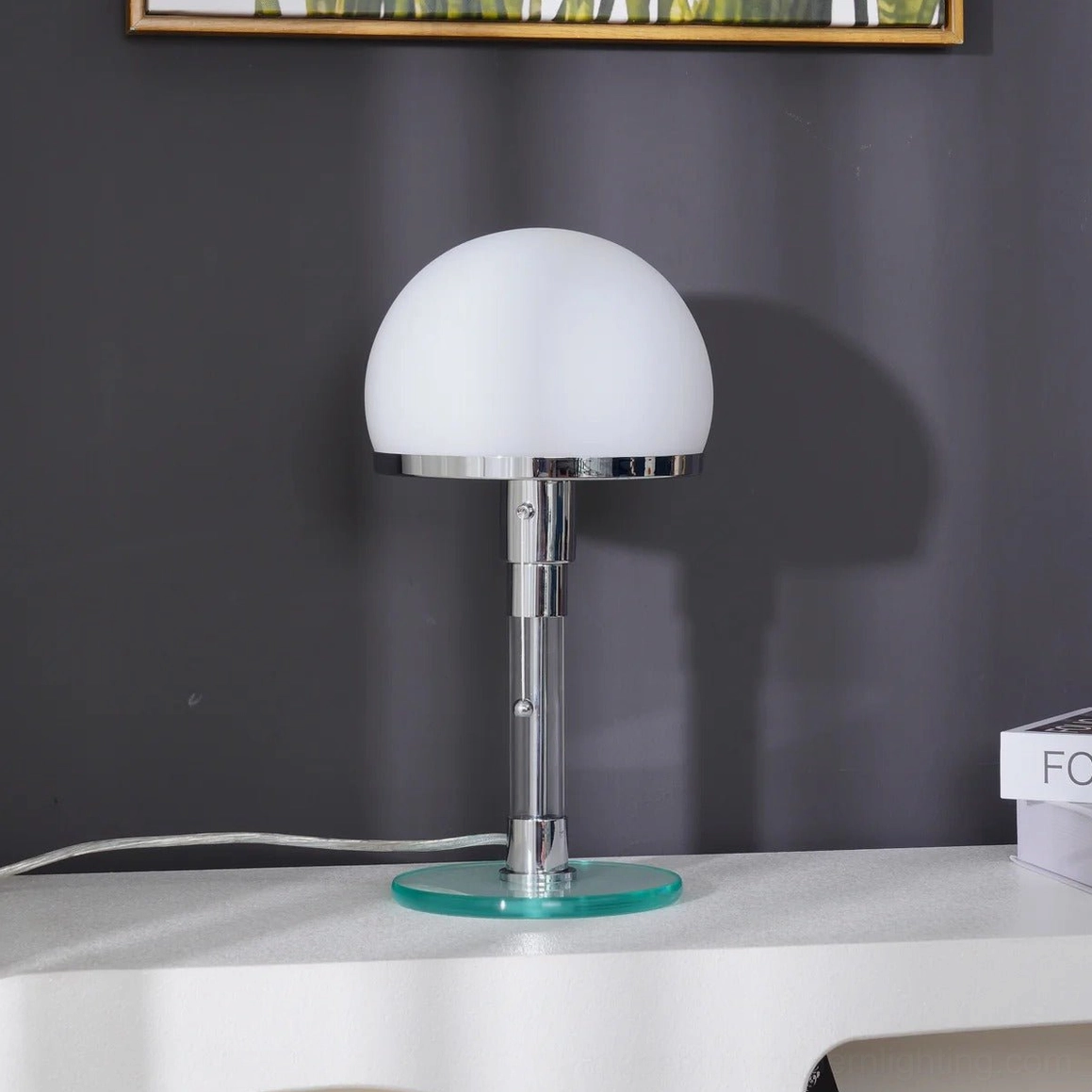 Unlit hemispherical chrome lamp on minimalist side table with neutral gray wall backdrop, clean modern design showcase