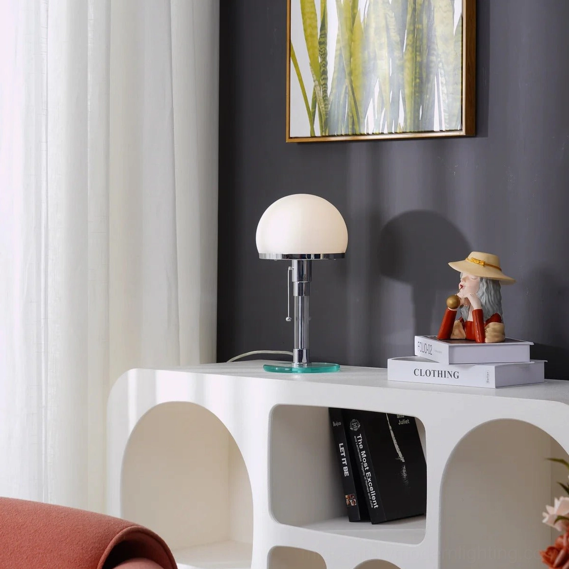 Unlit hemispherical chrome lamp on living room console table with stacked books and decorative figurine, minimalist styling