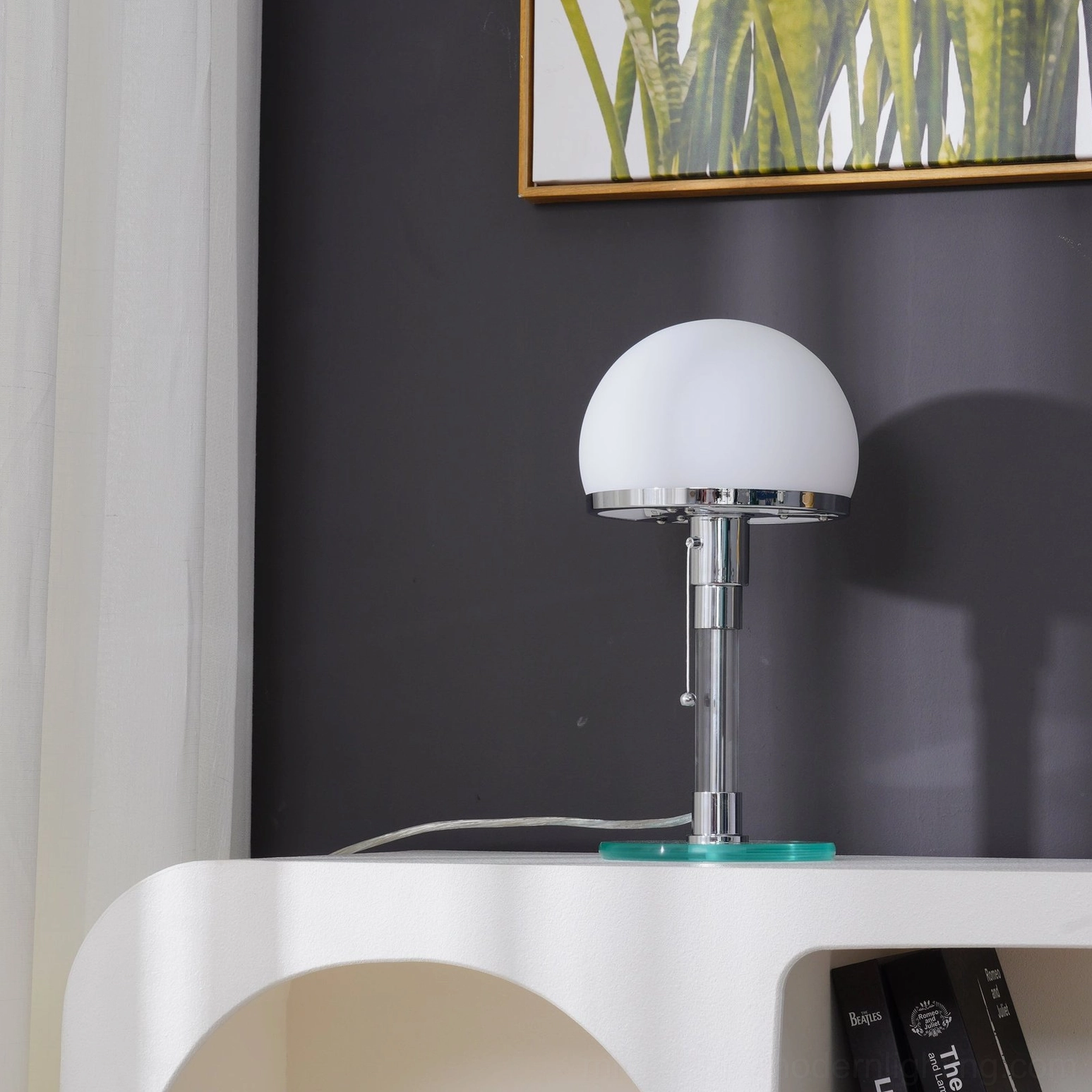 Chrome hemispherical table lamp viewed from side profile, modern sculptural form on living room console shelf with framed painting