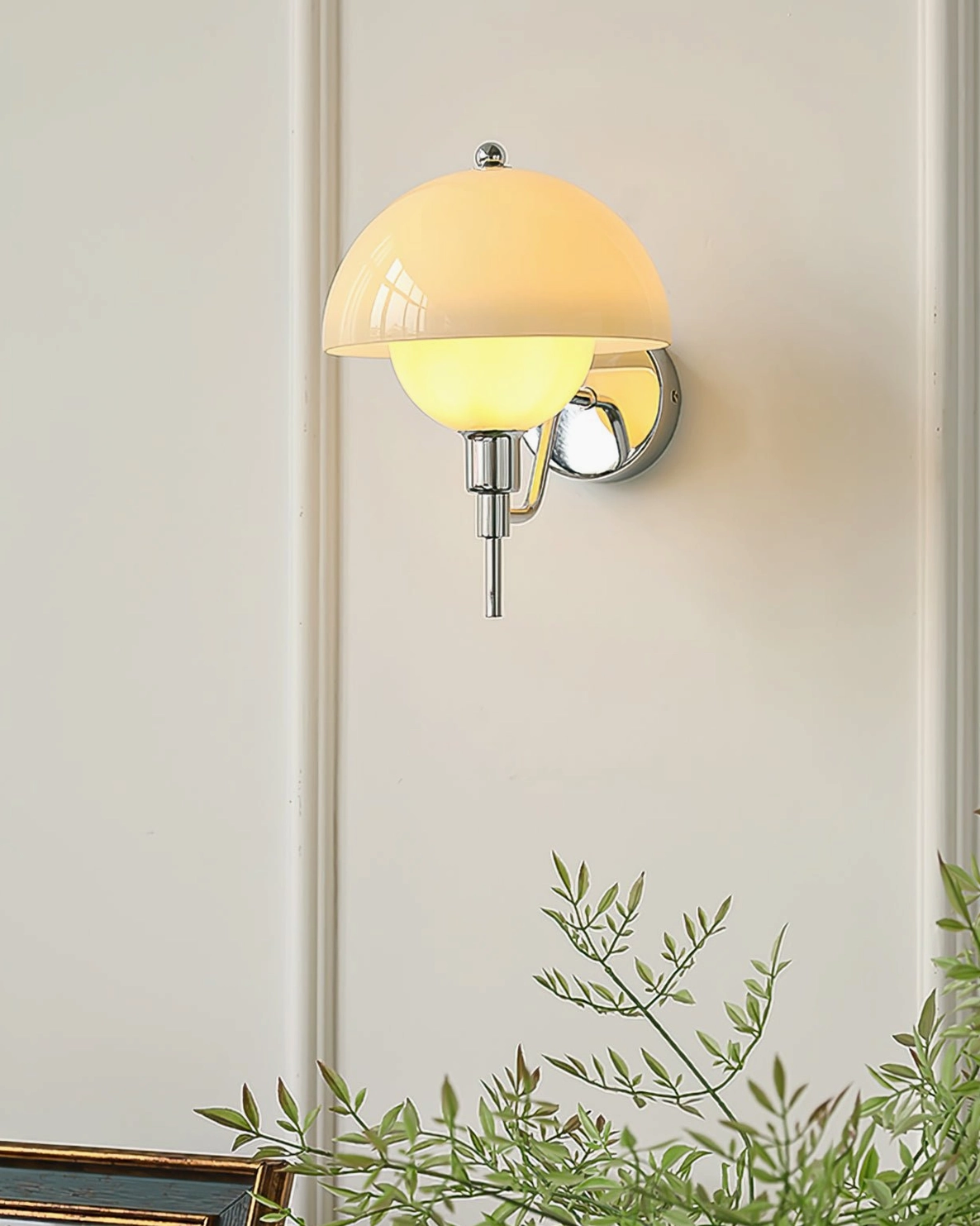 Close-up side view of chrome anchored orb wall lamp with amber glass on minimalist white wall with plant