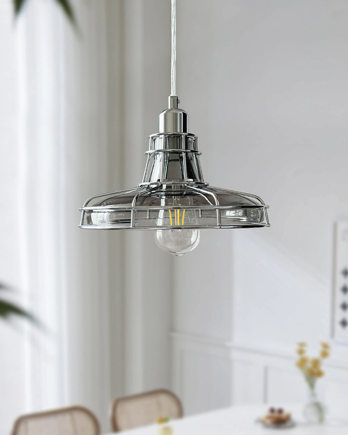 Chrome pendant light fixture installed above residential dining table, side overhead view showing compact cage design
