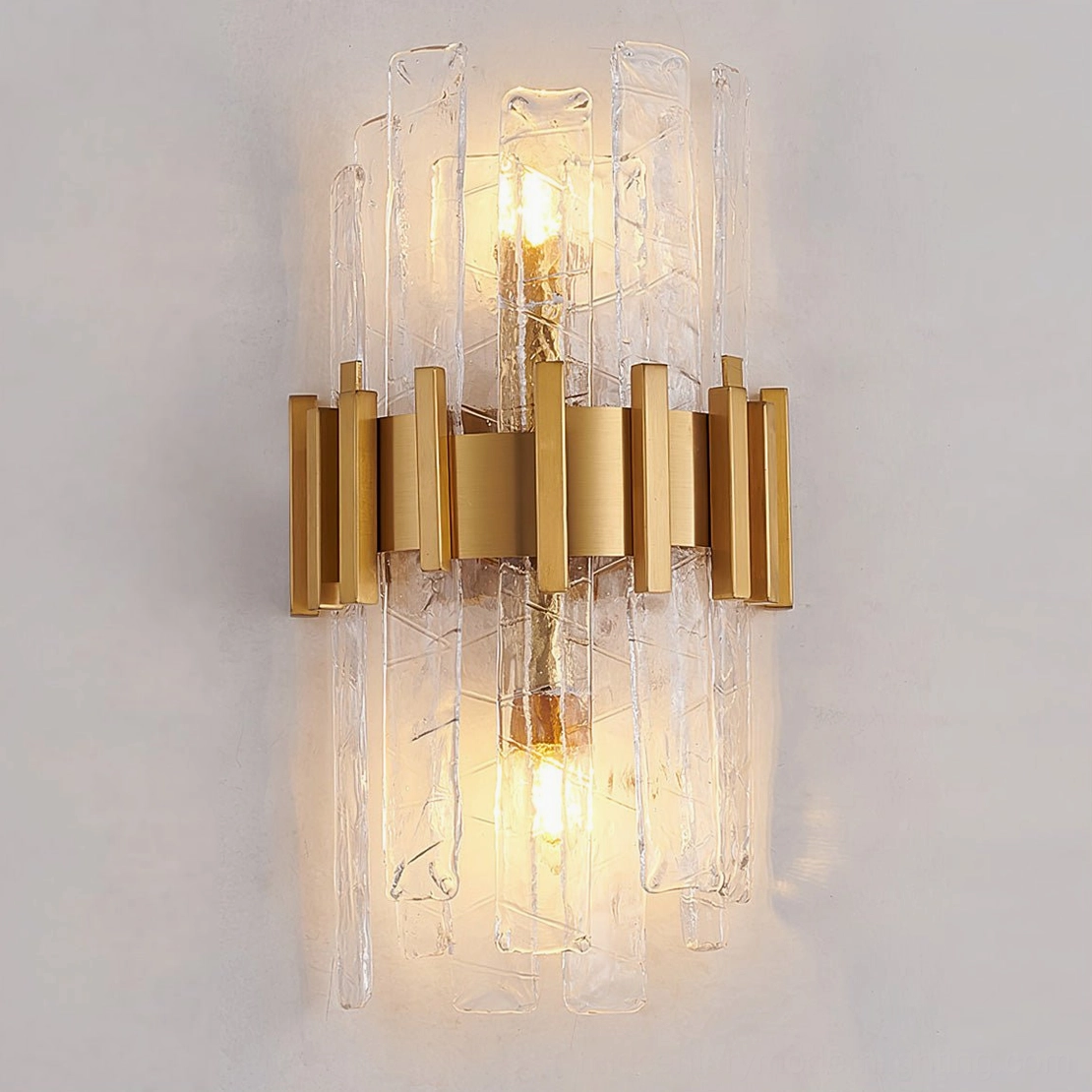 Modern gold wall sconce with rippled glass shades installed on beige interior wall, lit view