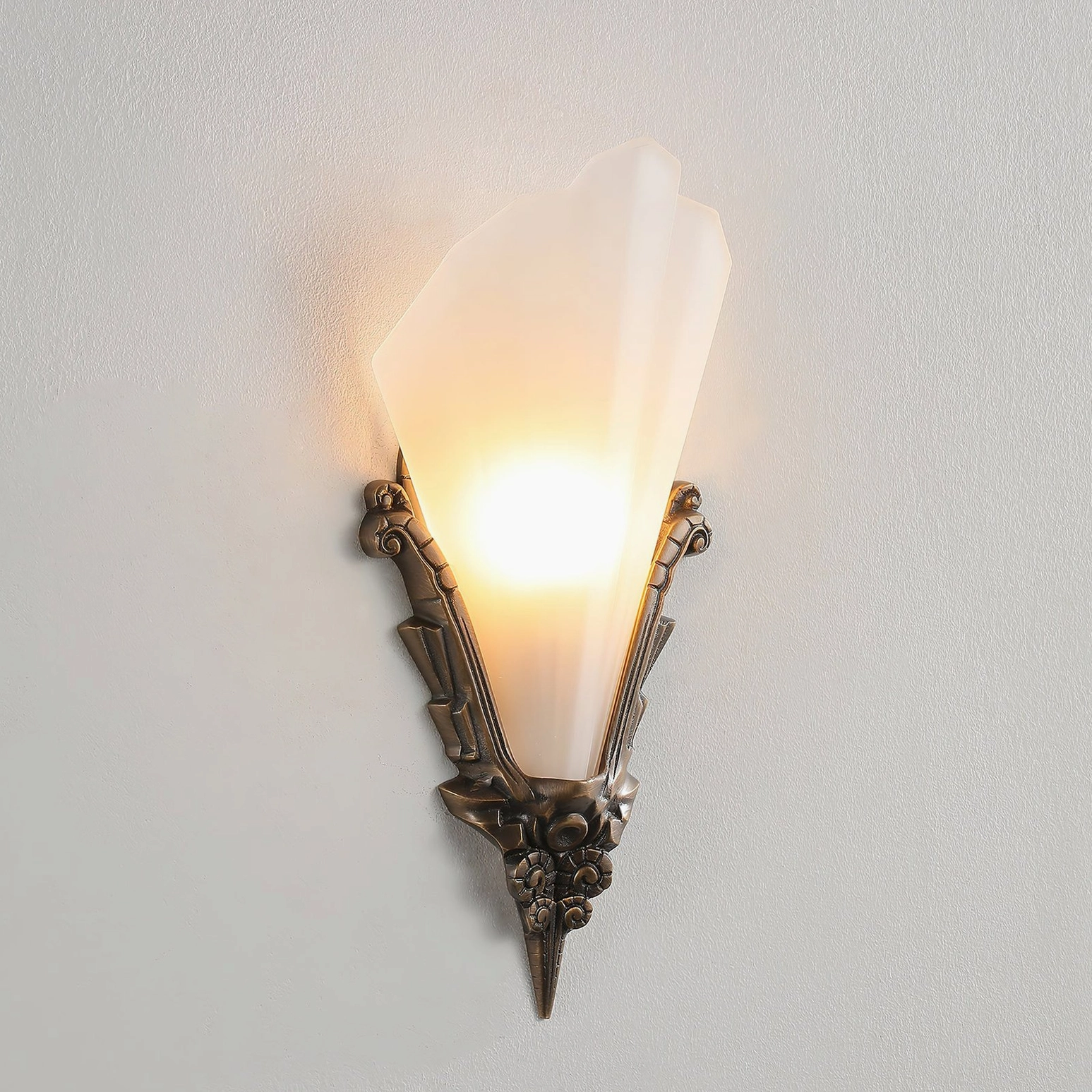 Claridge wall sconce lit from within showing wide frosted shade and ornamental brass framework
