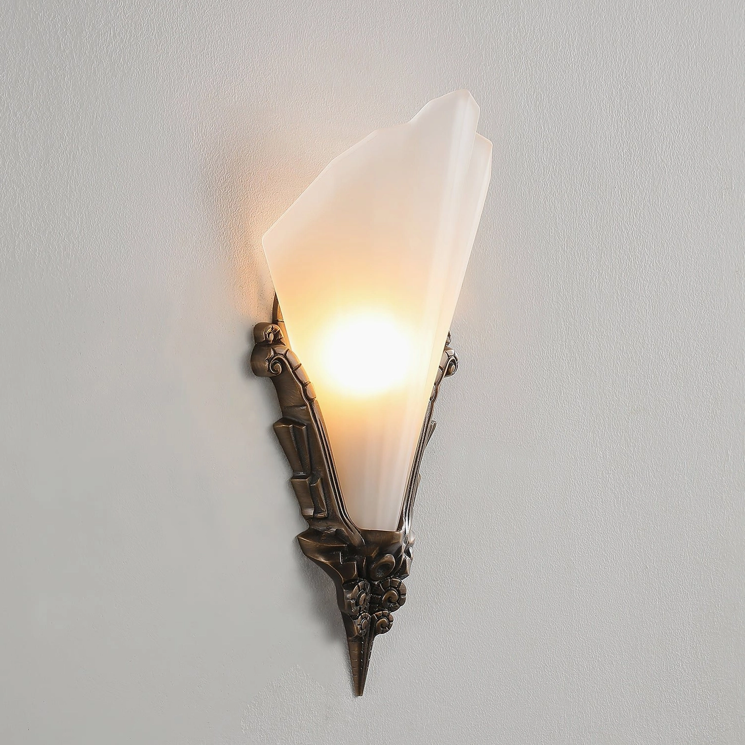 Illuminated Claridge Glass Wall Sconce showing diffused warm light through slim frosted shade and carved brass base